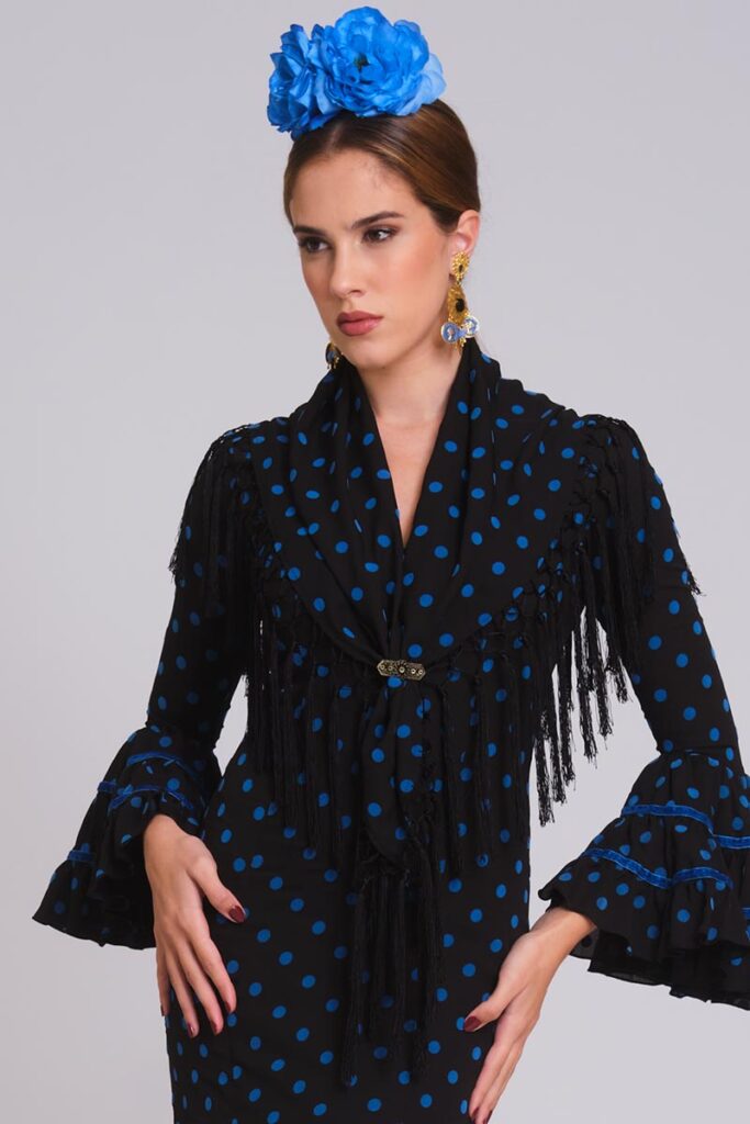 Vestido de flamenca negro con lunares azul eléctrico, mangas de volantes con terciopelo y mantoncillo de flecos negros.