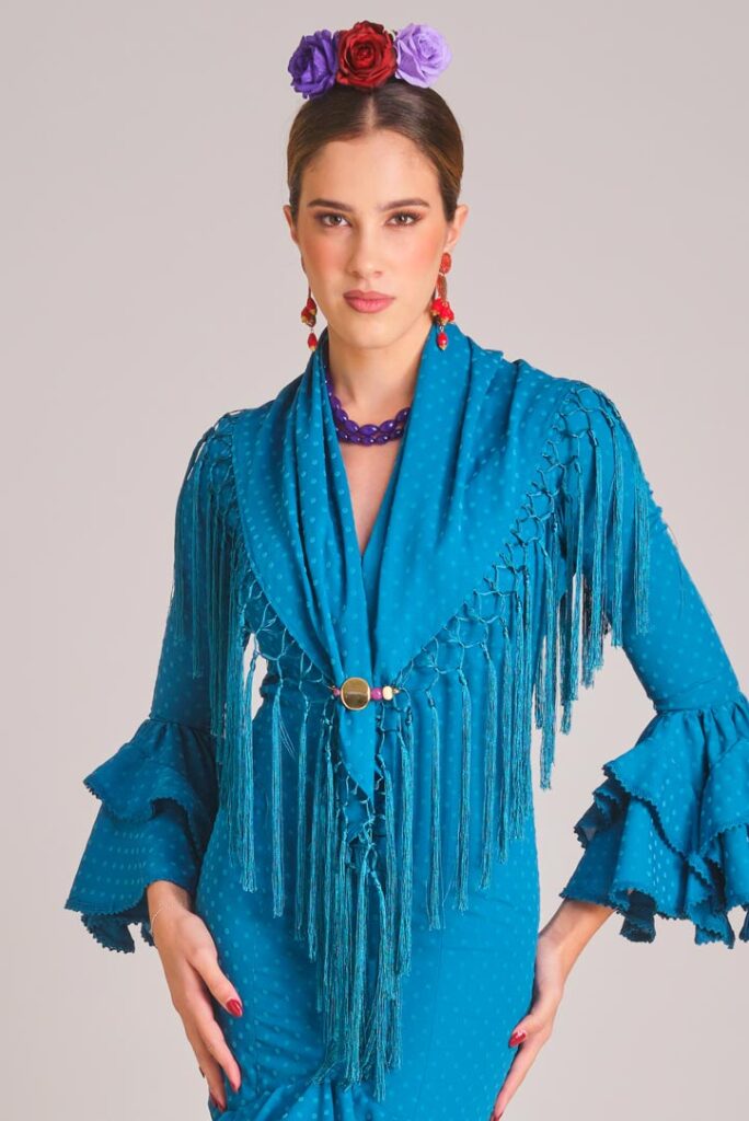 Vestido de flamenca azul turquesa con micropatrón de lunares al tono, mangas de doble volante y mantoncillo de flecos largos.