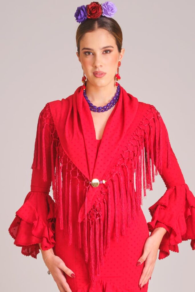 Vestido de flamenca rojo con micropatrón de lunares al tono, mangas con volantes dobles y mantoncillo de flecos largos.