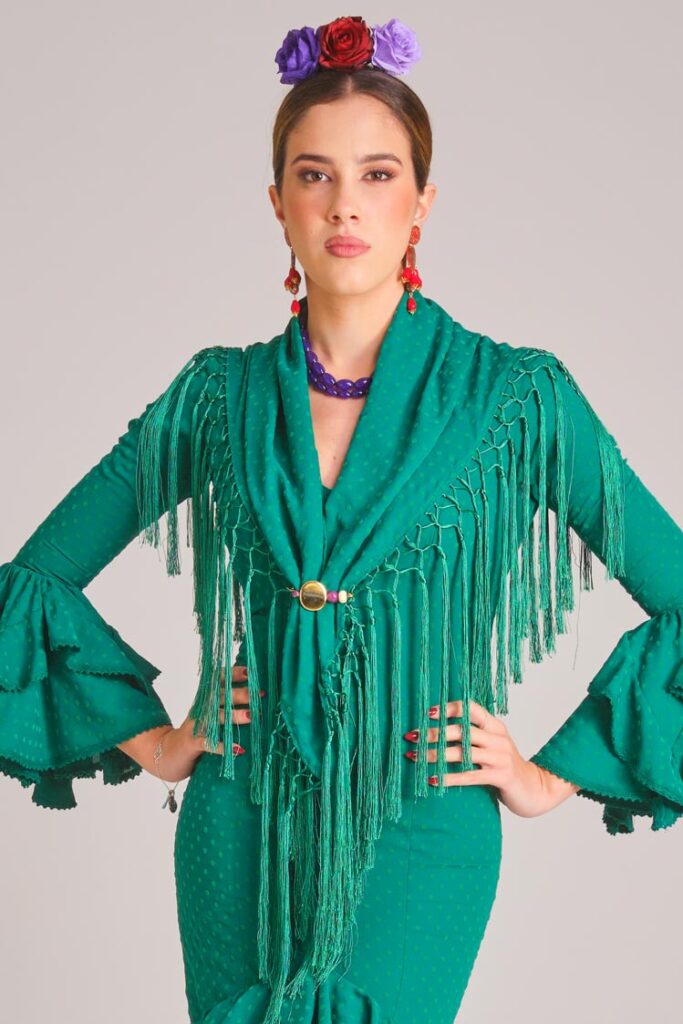 Vestido de flamenca verde esmeralda con microlunares al tono, mangas con volantes dobles y mantoncillo de flecos largos.