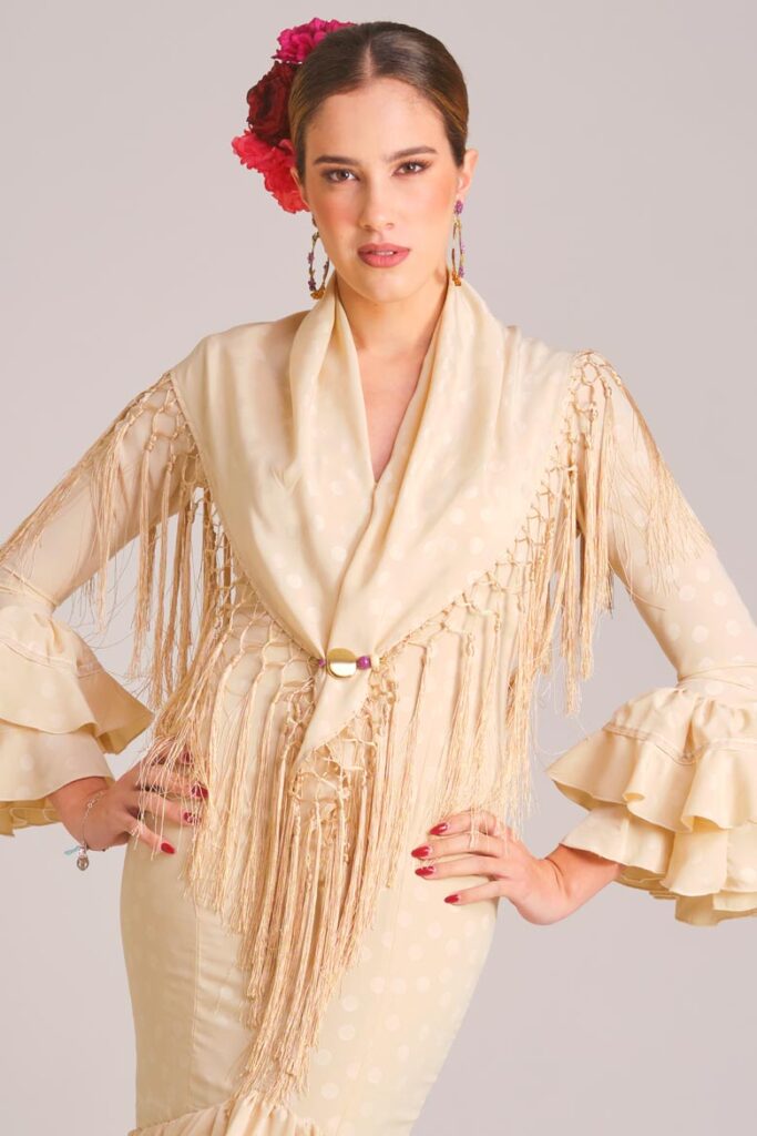 Vestido de flamenca beige con lunares marfil sutiles, mangas con volantes dobles y mantoncillo de flecos largos beige a juego.