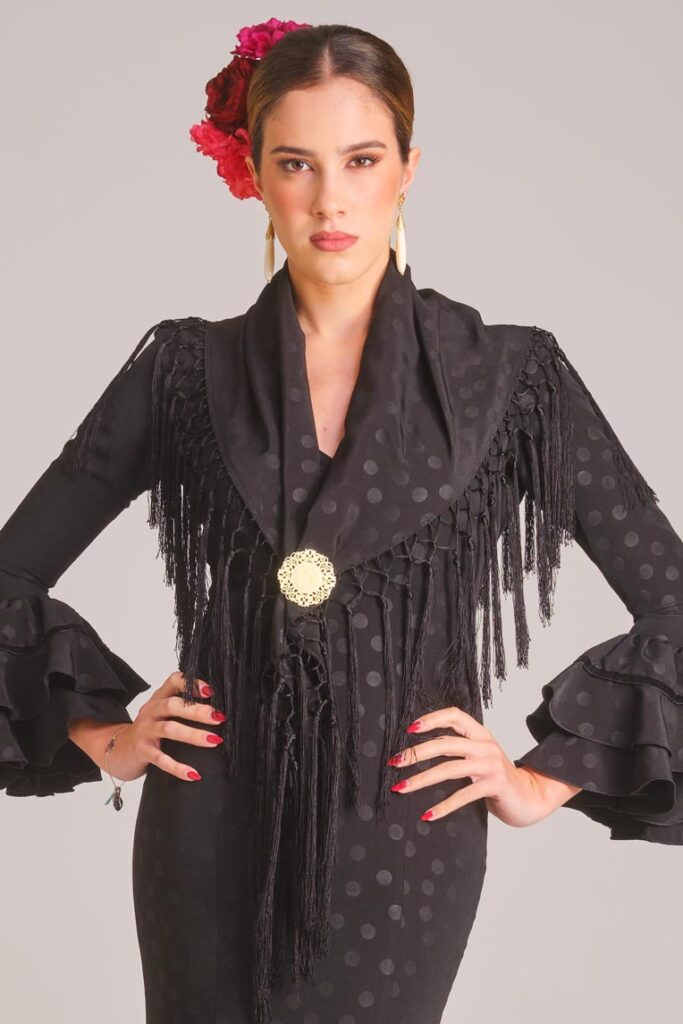 Vestido de flamenca negro con lunares al tono satinados, mangas con volantes dobles y mantoncillo de flecos negros a juego.