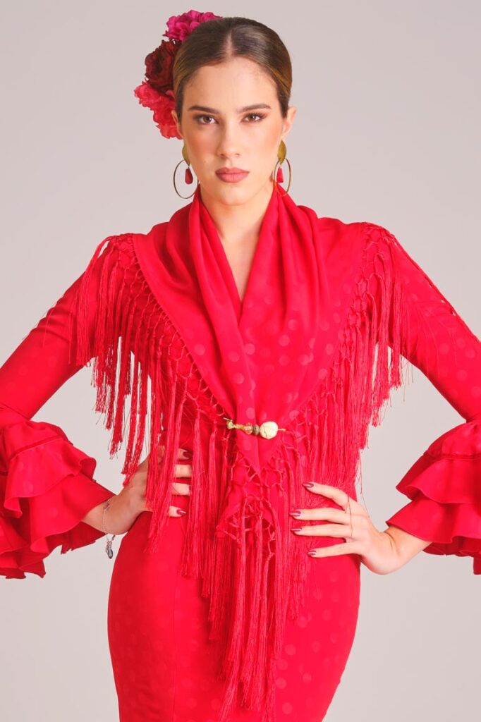 Vestido de flamenca rojo con lunares al tono texturizados, mangas con doble volante y mantoncillo de flecos largos a juego.