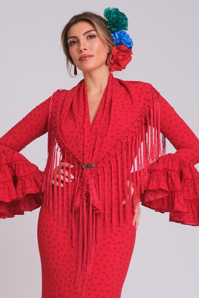 Vestido de flamenca rojo con lunares pequeños, mangas de faralaes con volantes y mantoncillo de flecos largos a juego.