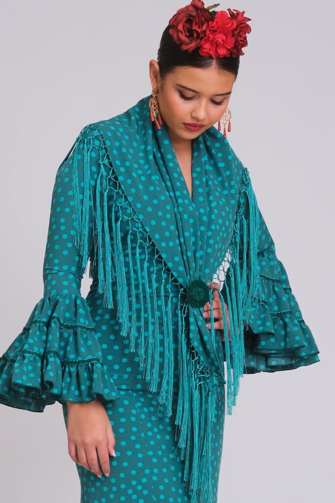 Vestido de flamenca verde botella con lunares turquesa, mangas con triples volantes y mantoncillo de flecos cruzado.