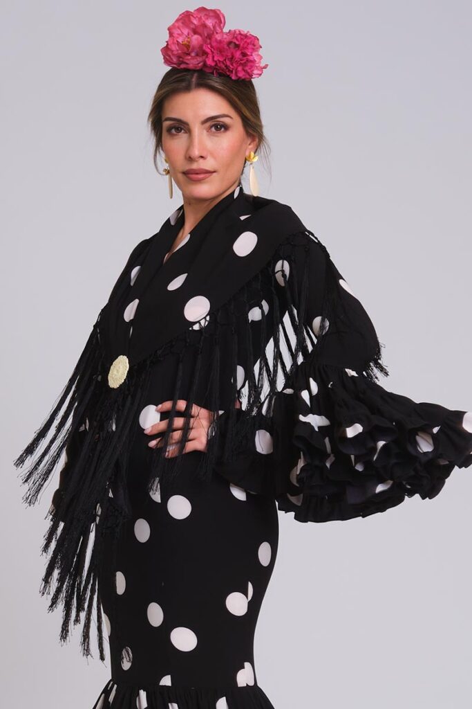 Traje de flamenca negro con lunares blancos, mantoncillo de flecos y volantes con volumen para feria