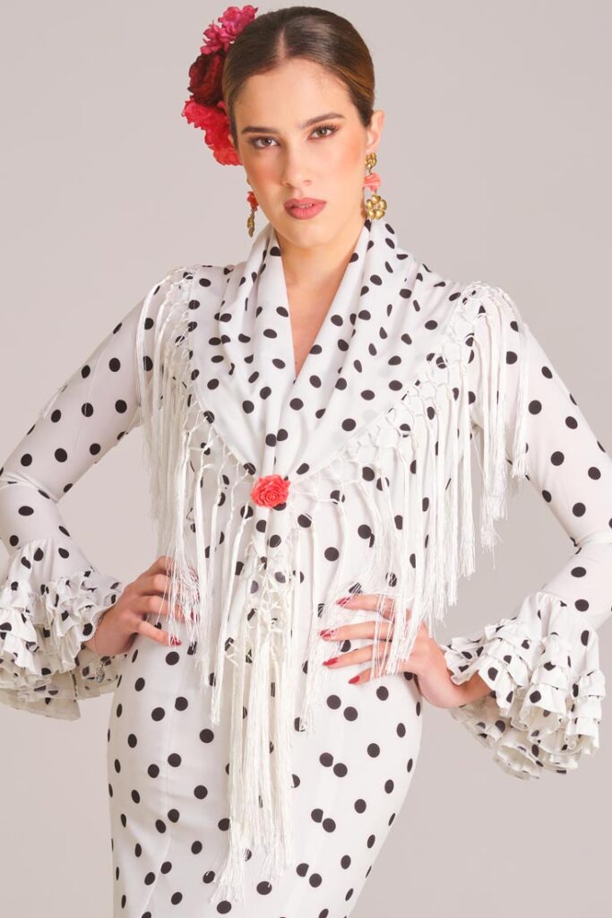 Traje de flamenca blanco con lunares negros, mantoncillo de flecos y volantes rizados para feria