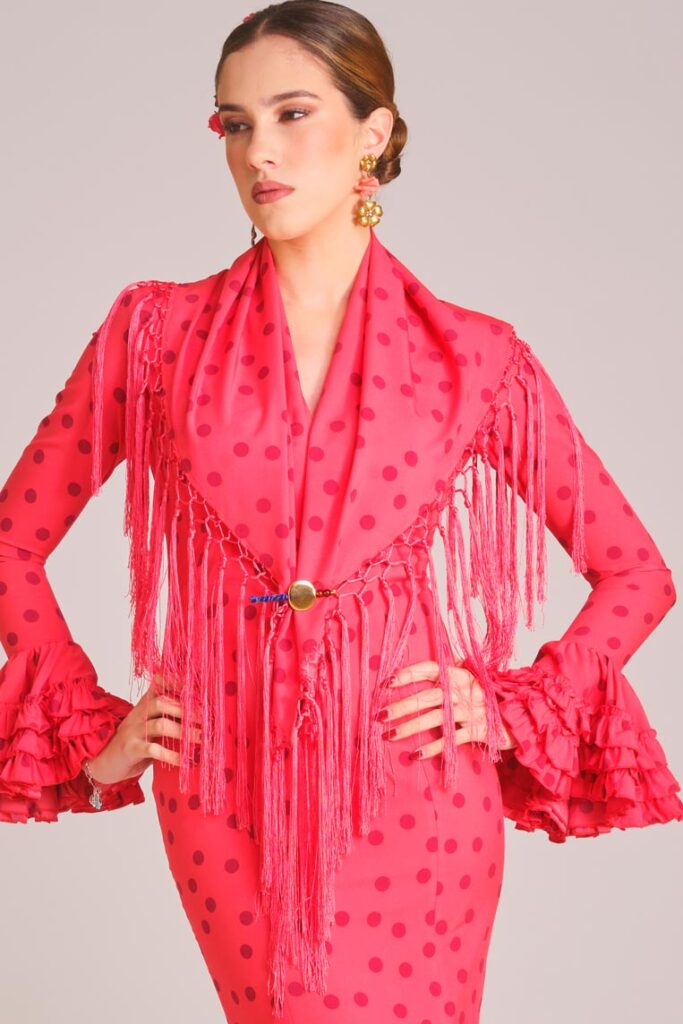 Traje de flamenca coral con lunares, mantoncillo de flecos y mangas con volantes para feria