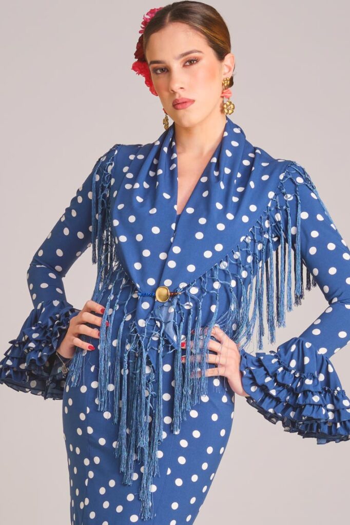 Traje de flamenca azul con lunares blancos, mantoncillo de flecos y volantes en cascada para feria