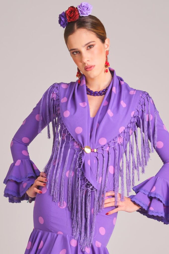 Traje de flamenca morado con lunares rosas, mantoncillo de flecos y mangas acampanadas para feria