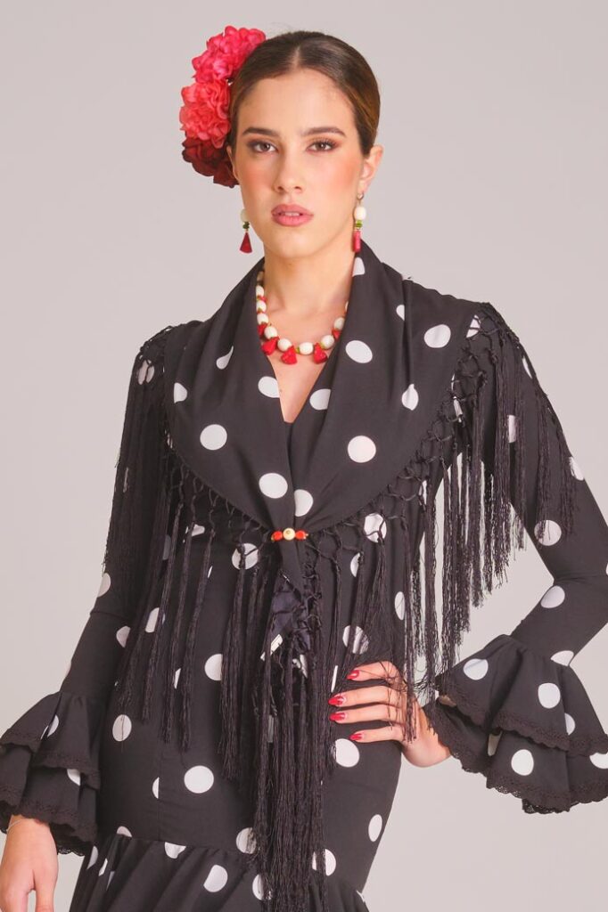 Traje de flamenca negro con lunares blancos, mantoncillo de flecos y mangas de volantes para feria