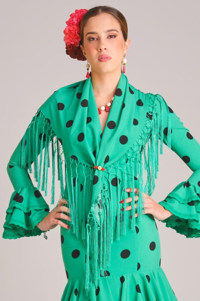 Traje de flamenca verde con lunares negros, mantoncillo de flecos y volantes para Feria de Abril