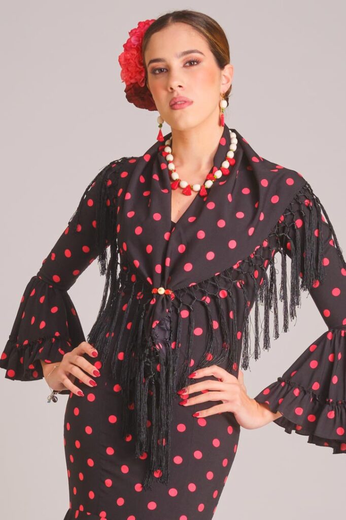 Traje de flamenca negro con lunares rosas, mantoncillo de flecos y mangas con volantes para feria