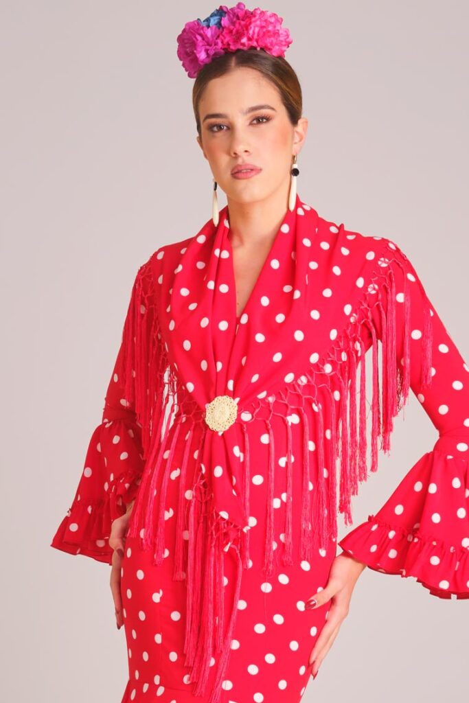 Traje de flamenca rojo con lunares blancos, mantoncillo de flecos y broche dorado para feria