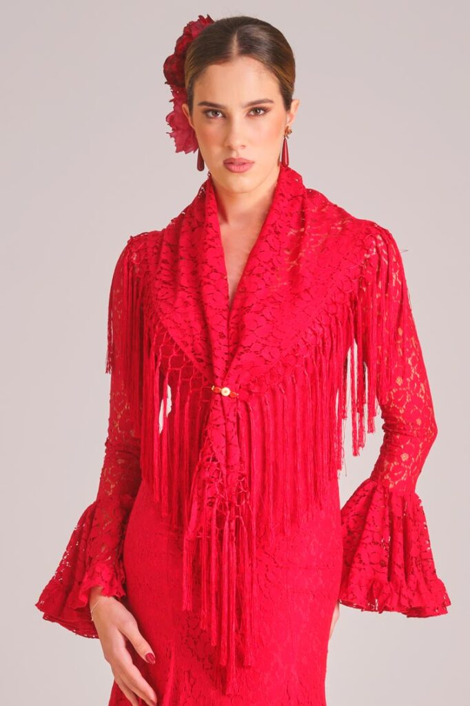 Traje de flamenca rojo de encaje con mantoncillo a juego y flecos para un look de feria sofisticado