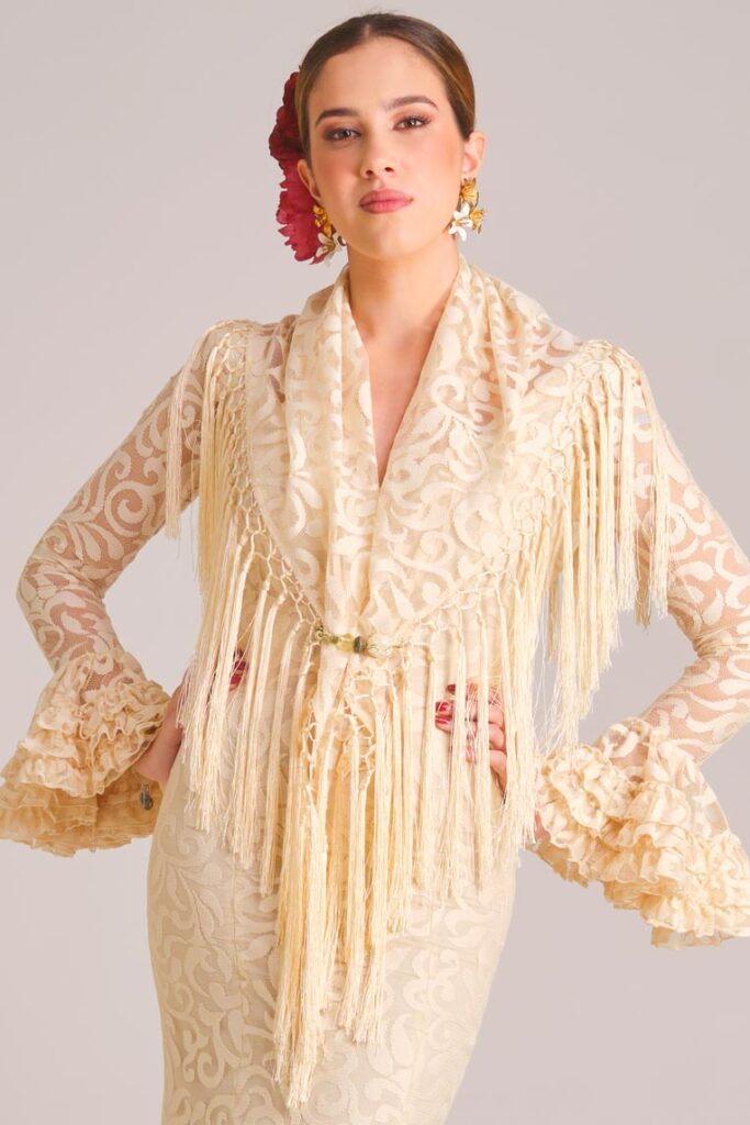 Traje de flamenca beige con encaje, mantoncillo a juego y flecos para un look de feria elegante