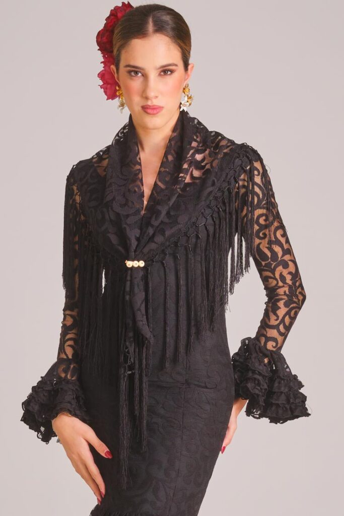 Traje de flamenca negro con encaje, mantoncillo a juego y flecos para un look de feria elegante