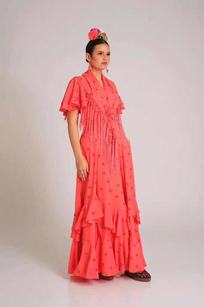Traje de flamenca coral con lunares, mantoncillo a juego y volantes para Feria de Abril