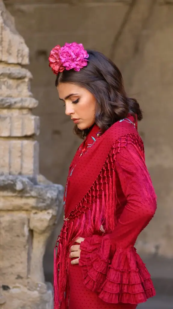 Mujer con traje de flamenca rojo, flores en el cabello y flecos