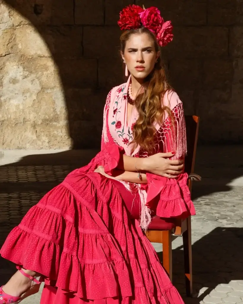 Mujer con traje de flamenca rosa, flores rojas en el cabello, posando con una actitud elegante