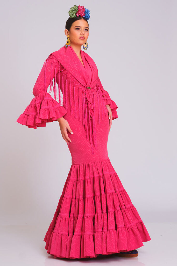 Traje de flamenca fucsia con estampado sutil de lunares, diseño entallado con volantes en falda y mangas, ideal para ferias y eventos andaluces