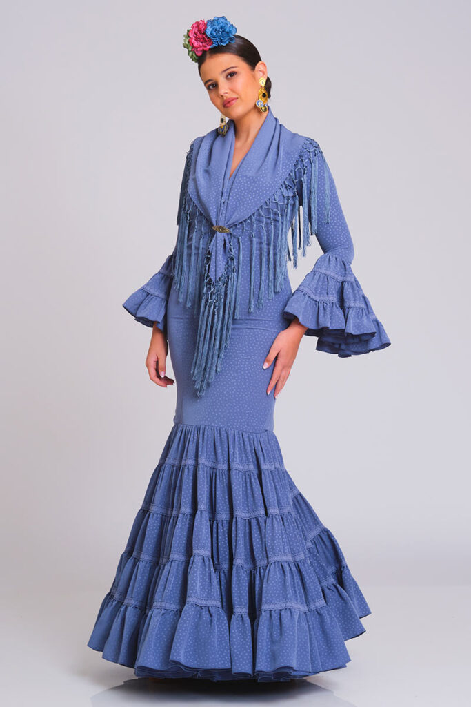Traje de flamenca azul grisáceo con estampado sutil de lunares, diseño entallado con volantes en falda y mangas, ideal para ferias y eventos andaluces